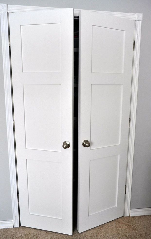 two white doors open in a room with carpeted flooring and gray wall behind them