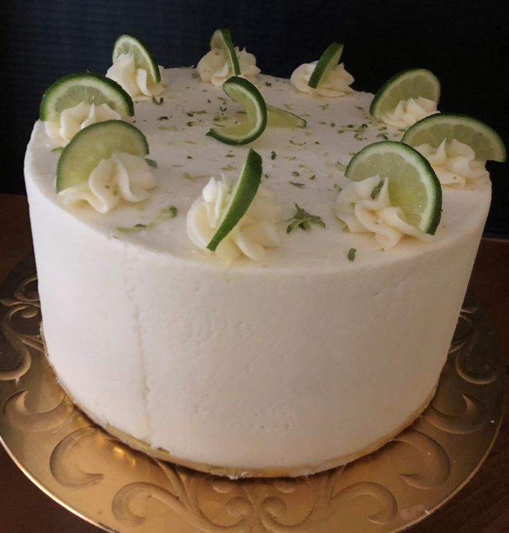 a white cake with limes and cucumbers on top sits on a gold plate