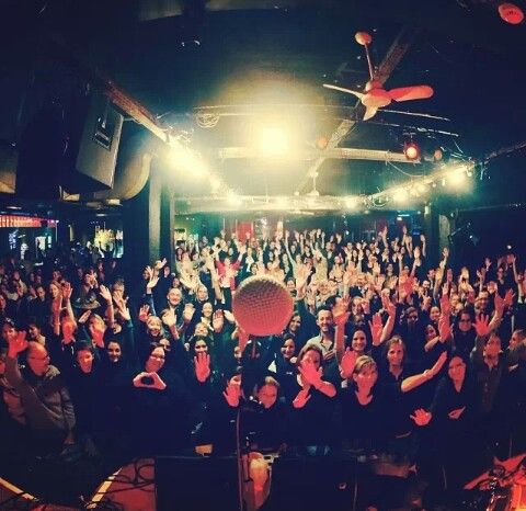 a large group of people sitting in front of a microphone on stage with their hands up