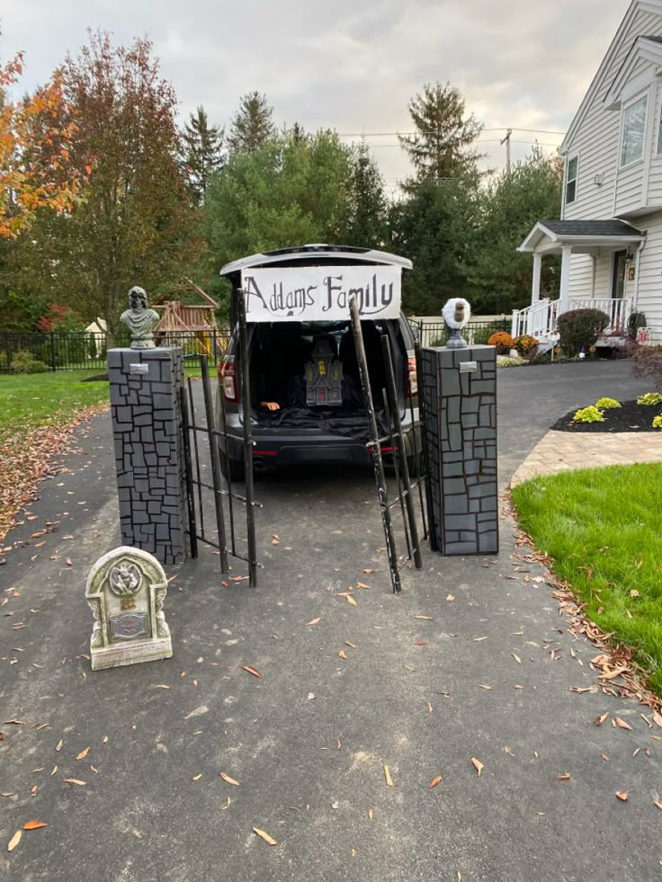 a car parked in front of a house with halloween decorations on the driveway and gate