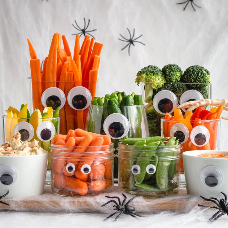 a table topped with bowls filled with carrots and veggies covered in googly eyes