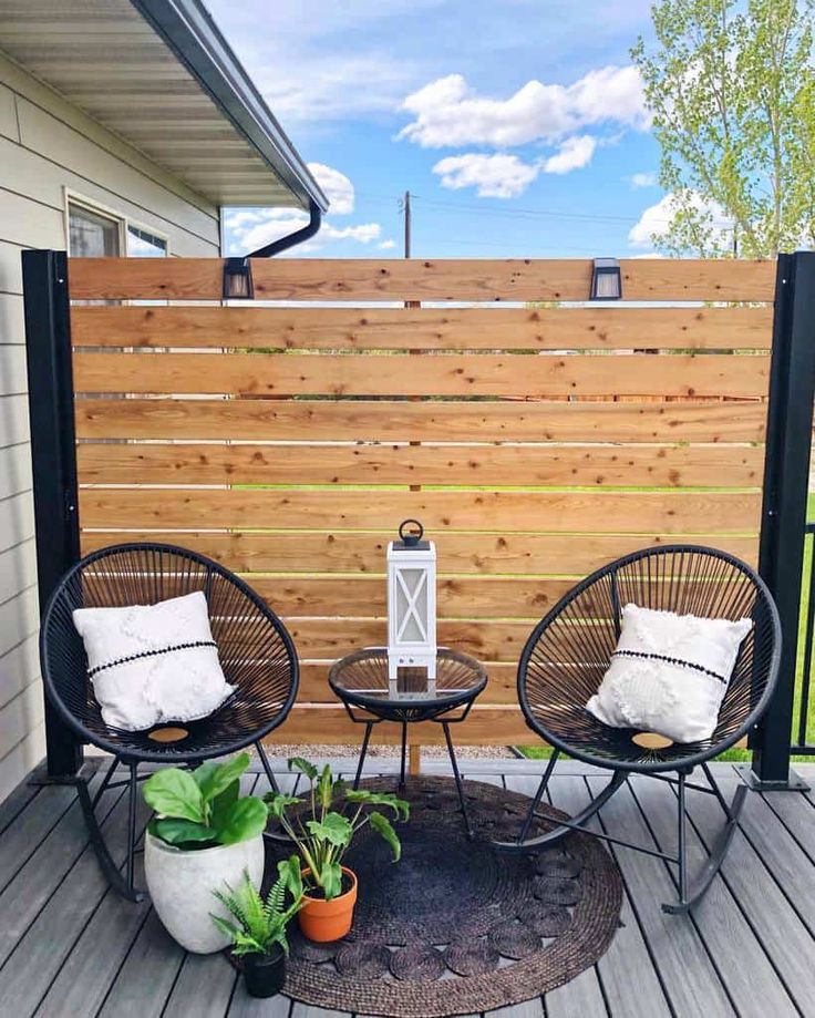 two chairs sitting on top of a wooden deck next to a potted plant in front of a fence