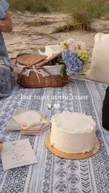 a white cake sitting on top of a table next to a basket filled with flowers