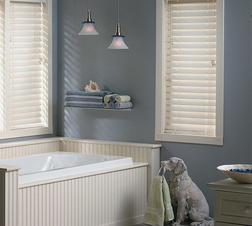 a white bath tub sitting next to two windows with blinds on the window sill