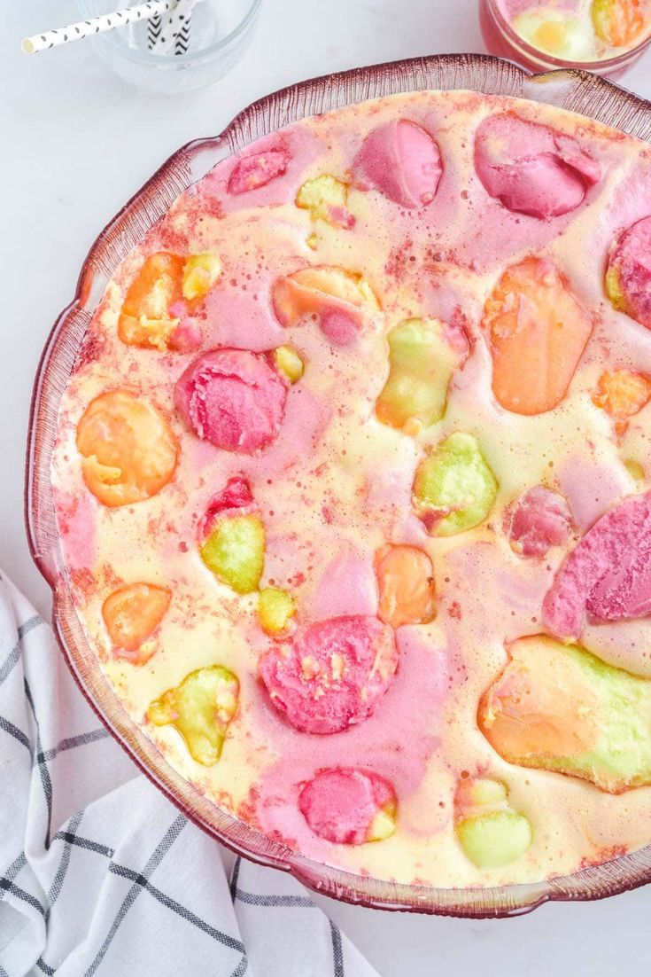 a pizza with different colored toppings sitting on top of a table next to two glasses