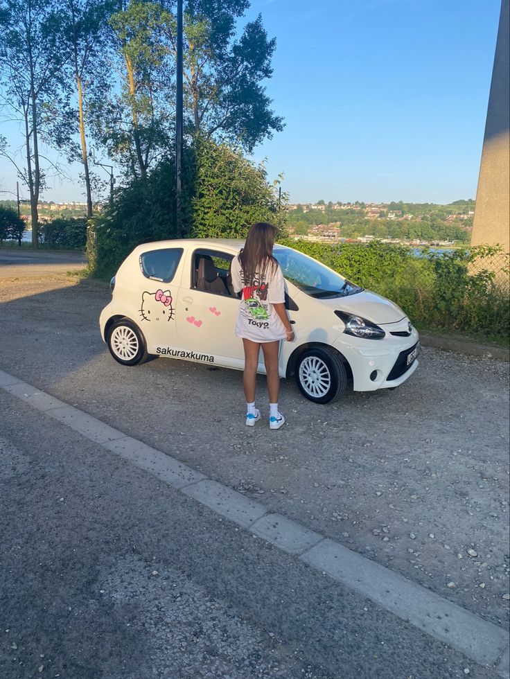 a woman standing next to a small white car