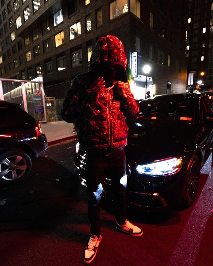 a man standing on the side of a road next to a parked car at night