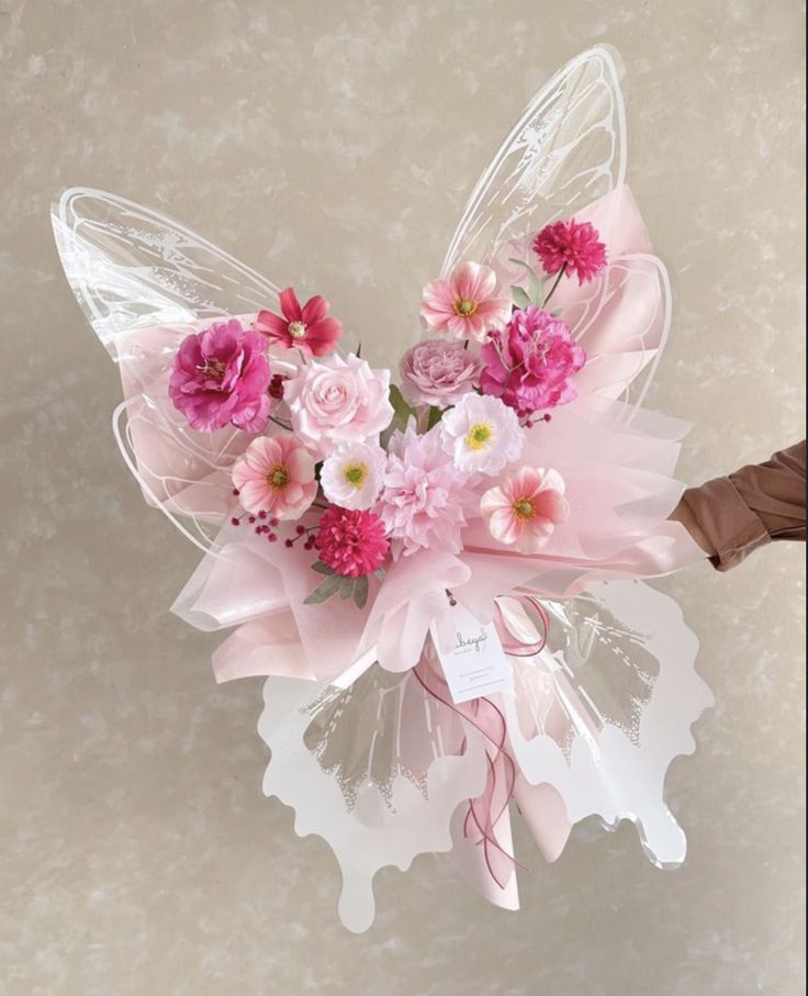 a hand holding a bouquet of pink flowers and butterfly wings with a tag on it