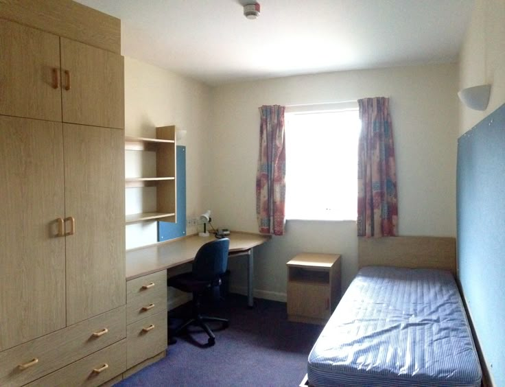 a bedroom with a bed, desk and cupboards in front of a large window