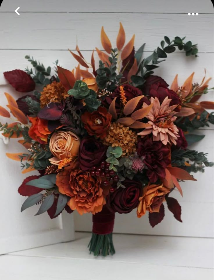 the bridal bouquet is made up of flowers and leaves, including oranges and burgundy