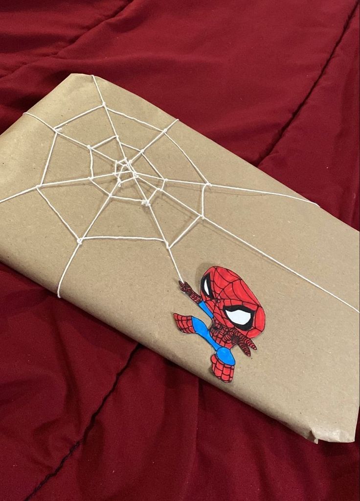 a spiderman wrapped in brown paper on top of a red bed sheet with white thread