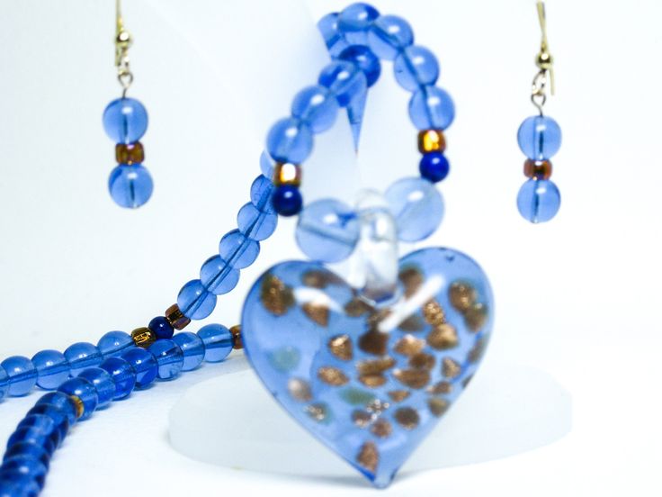 Austin Hamilton blue glass heart-shaped pendant with gold random shapes on cornflower blue glass round bead necklace earring set 14K gold-filled. 18-inch glass necklace glass heart pendant earring set 14K gold-filled. The round cornflower blue beads are 6 mm. The gold tone cylindrical rondelles are 3 x 3 mm. There are four 4mm lapis beads in the necklace. The 14K gold-filed lobster clasp is 11 mm.  The heart shaped pendant is 1.2 inches wide x 1.2 inches long.  The earrings are on 14K gold-filled earwires and have a 0.6-inch drop. Elegant Blue Jewelry With Heart Beads, Blue Heart-shaped Jewelry With Heart Beads, Blue Heart Beads Heart-shaped Jewelry, Blue Heart Pendant Jewelry Gift For Her, Glass Heart Beads Jewelry, Blue Necklace With Heart Charm, Blue Necklaces With Heart Charm And Round Shape, Blue Necklace With Round Heart Charm, Blue Glass Jewelry With Heart Beads