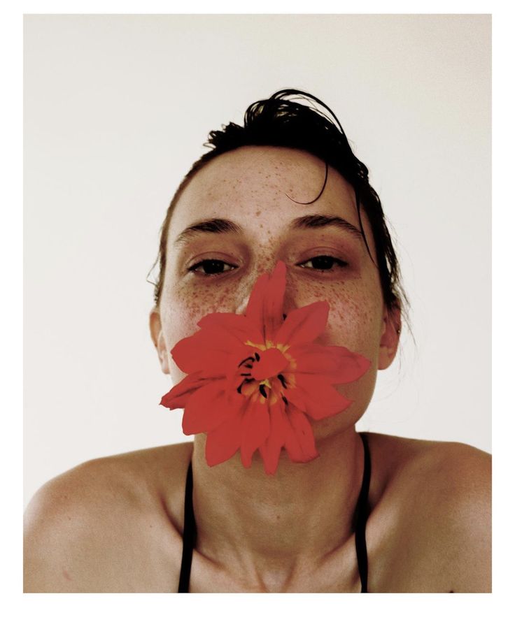 a woman with freckles on her face holding a flower in front of her mouth