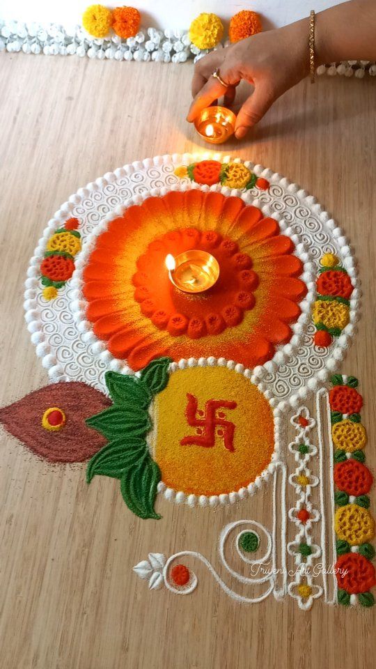 a woman is decorating the floor with colorful flowers and leaves on it, while holding a lit candle in her hand