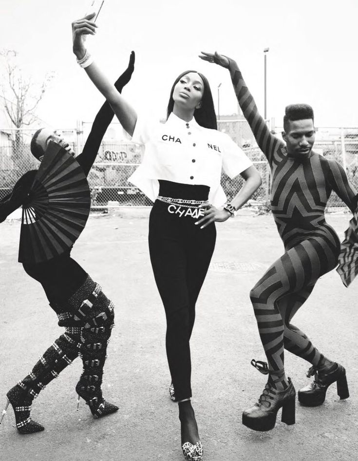 three people in striped outfits are dancing on the street with their hands up and one is holding her head