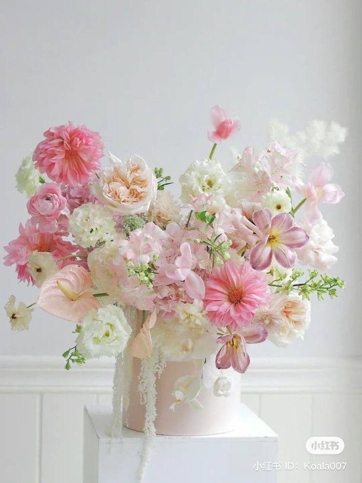 a white vase filled with lots of pink and white flowers on top of a table