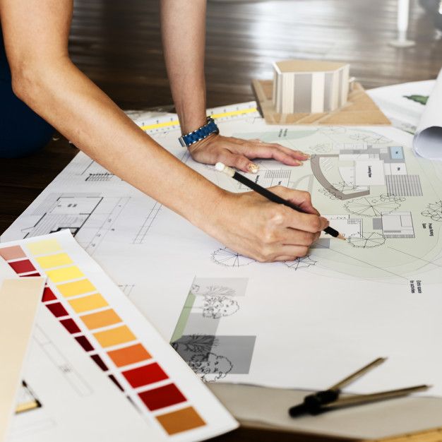 two people working on architectural drawings at a table with color swatches and paintbrushes