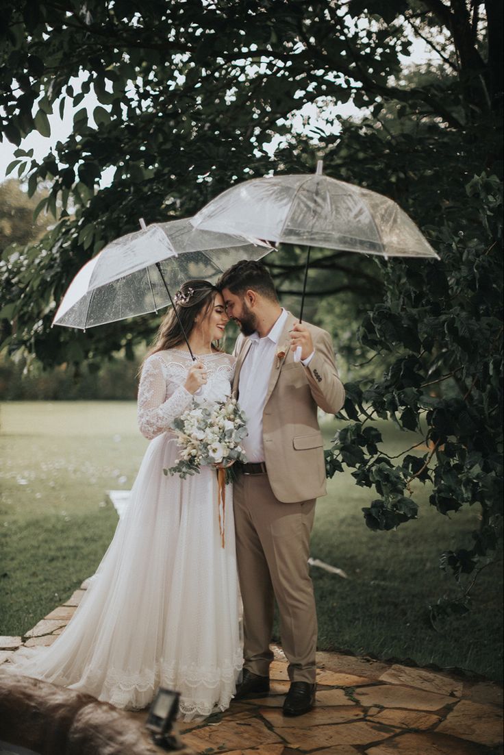 a bride and groom standing under umbrellas in the rain