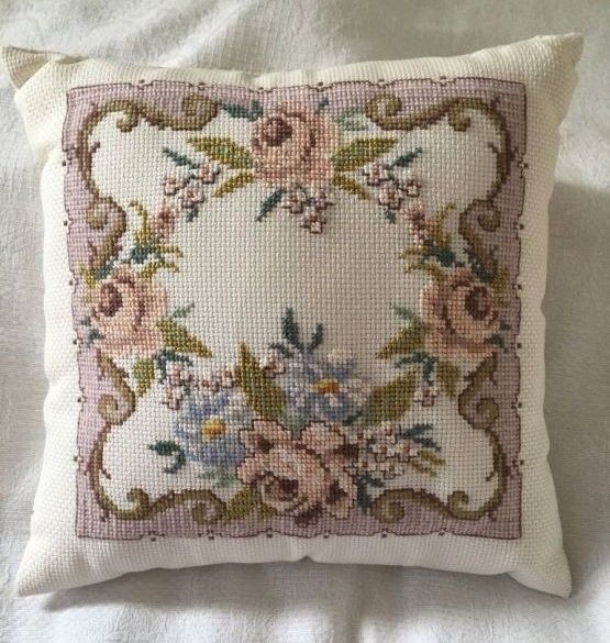 an embroidered pillow with flowers on it sitting on a white bed sheet in front of a mirror