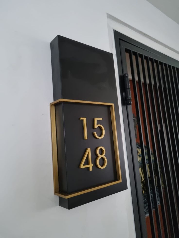 a black and gold house number sign mounted to the side of a white wall next to a door