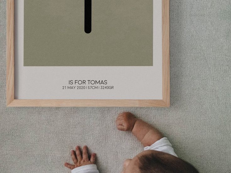 a baby laying on the floor next to a framed poster with a cross in it