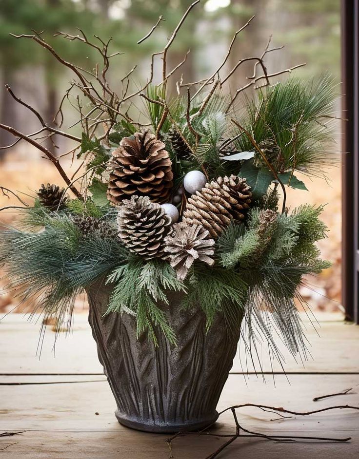 a vase filled with pine cones and greenery sitting on top of a wooden table