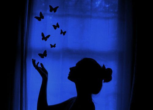 a woman standing in front of a window with butterflies coming out of her hands,