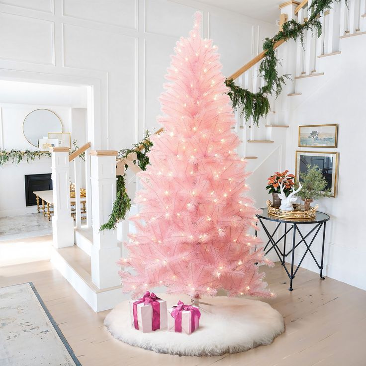 a pink christmas tree with presents on the floor next to it and stairs in the background