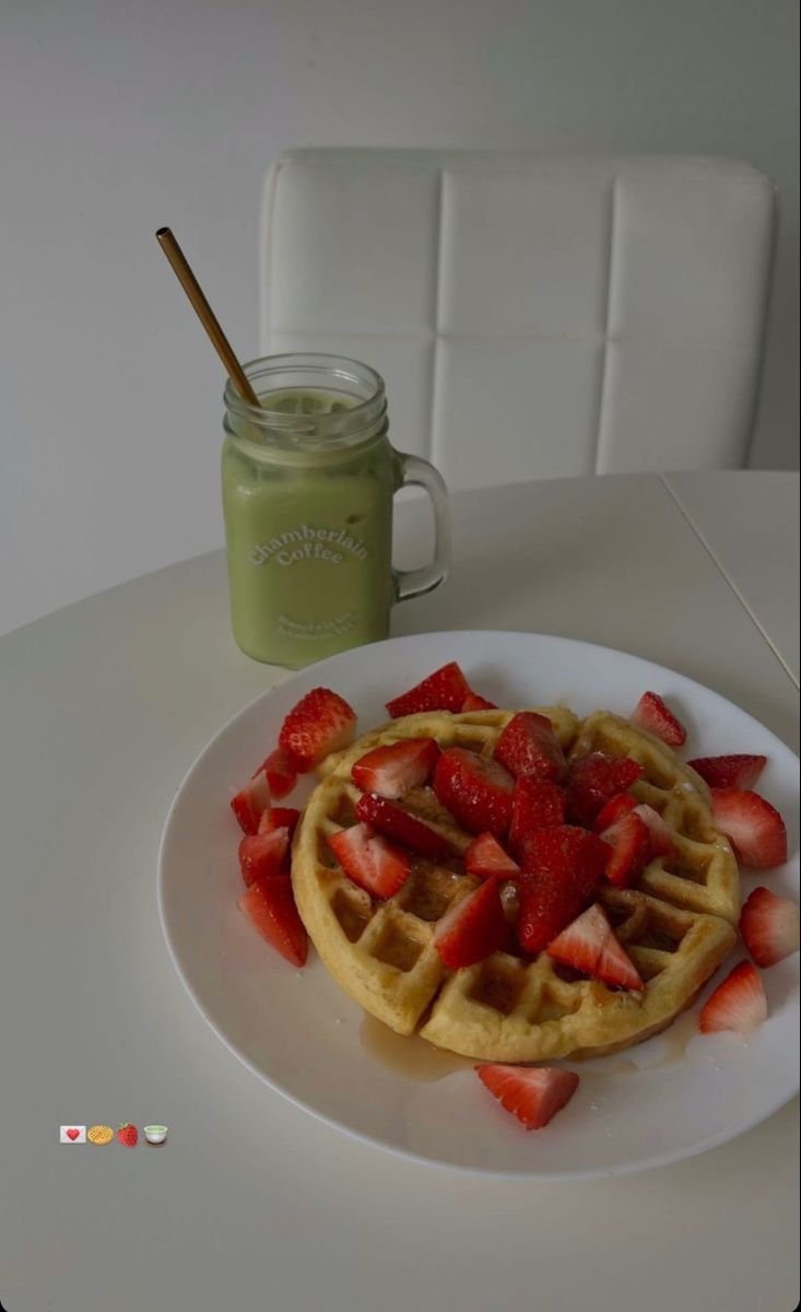 a white plate topped with waffles and strawberries next to a mason jar