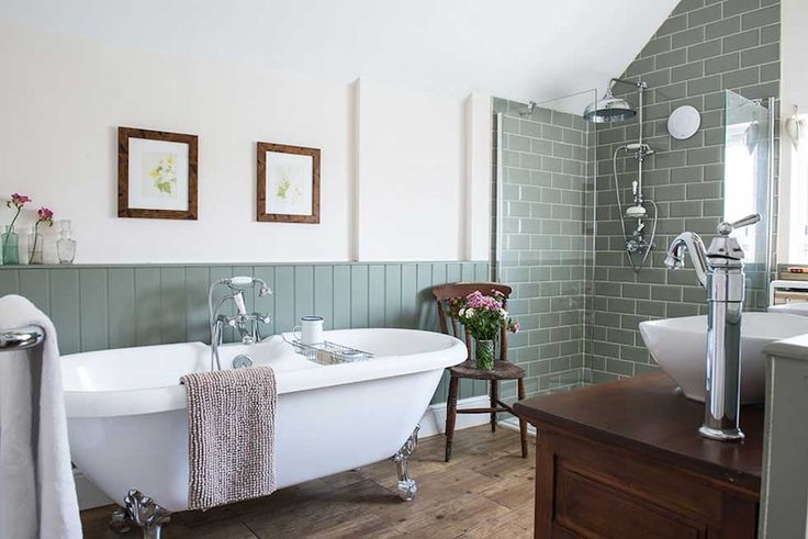 a white bath tub sitting next to a wooden counter top in a bathroom with green tiles on the walls