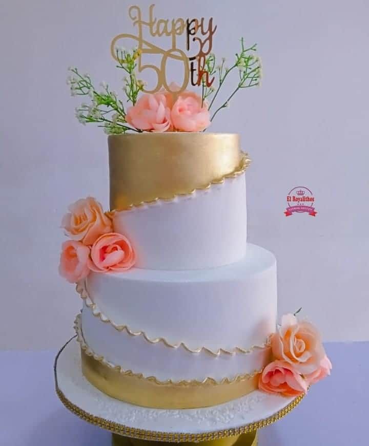 a white and gold wedding cake with pink flowers on the top tier is decorated with a happy 50th sign