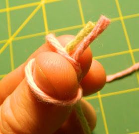 a hand holding a piece of yarn on top of a green table next to a pair of scissors