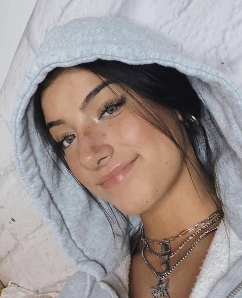 a woman wearing a gray hoodie with a white blanket over her head and necklaces on