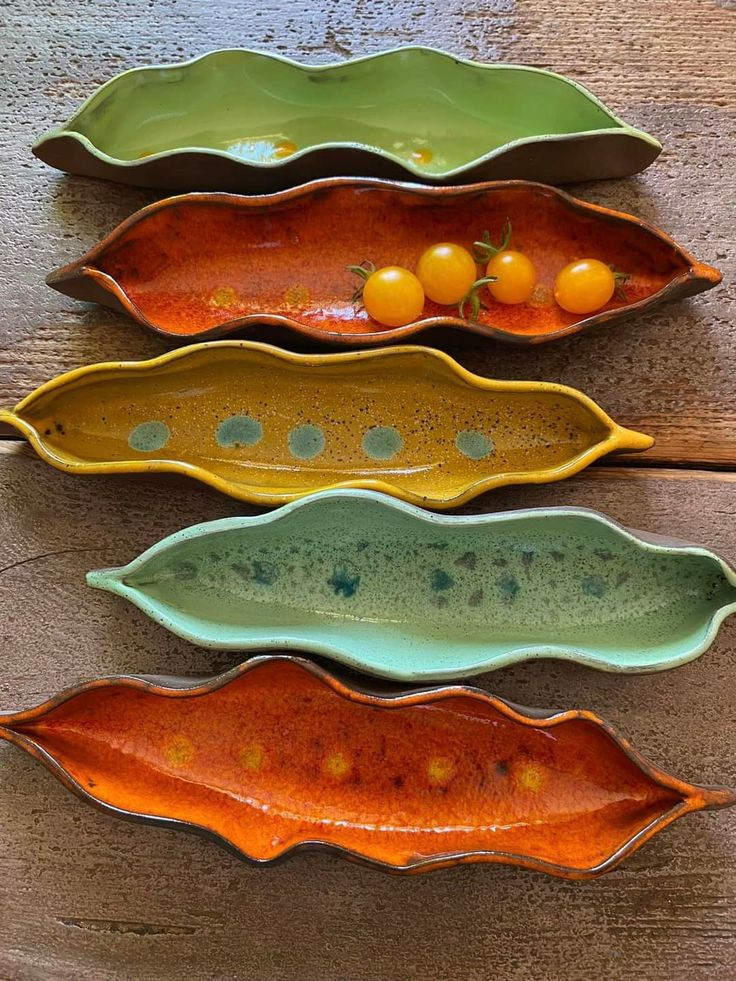 three different shaped dishes sitting on top of a wooden table next to oranges and tomatoes