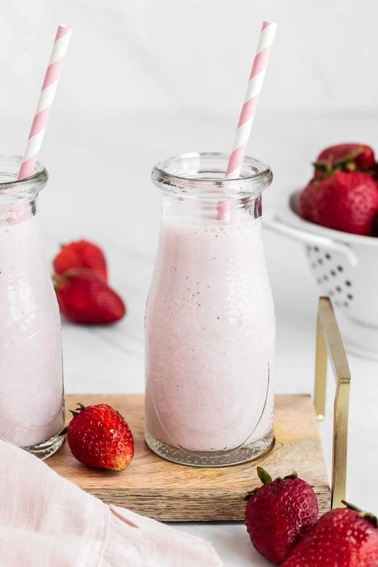 two mason jars filled with strawberry milk next to strawberries