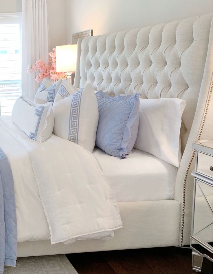 a white bed topped with lots of pillows next to a night stand and window sill