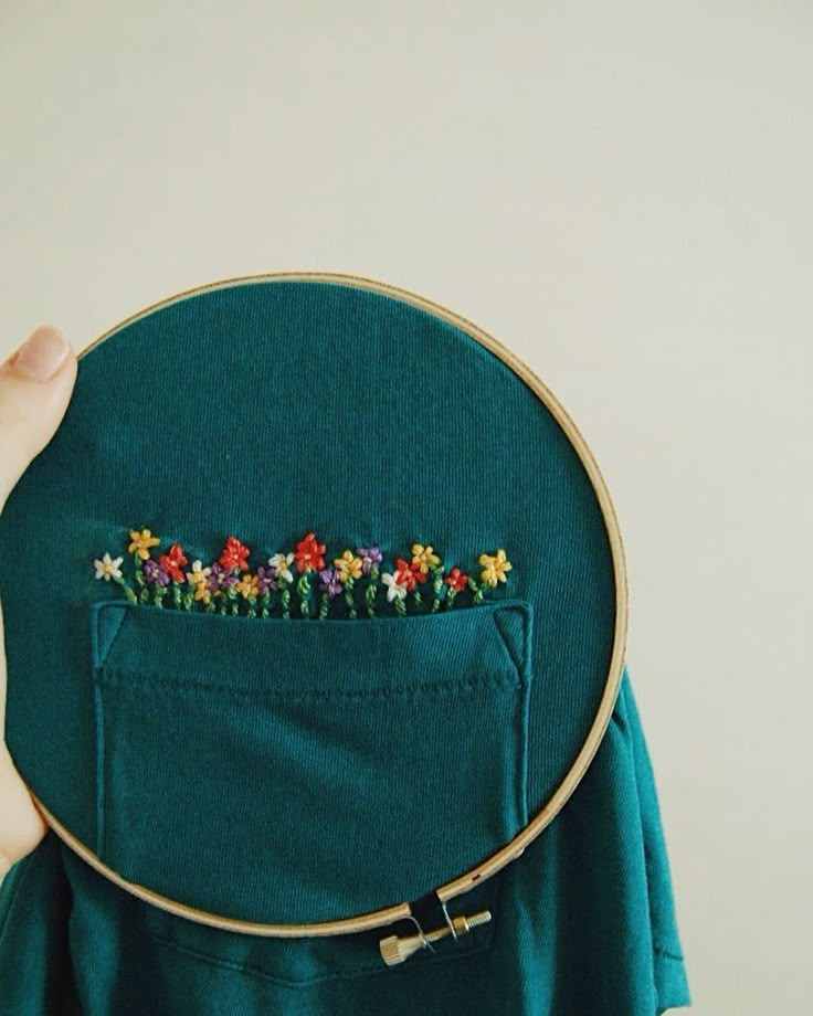 a person holding up a green piece of cloth with flowers in the pocket on it