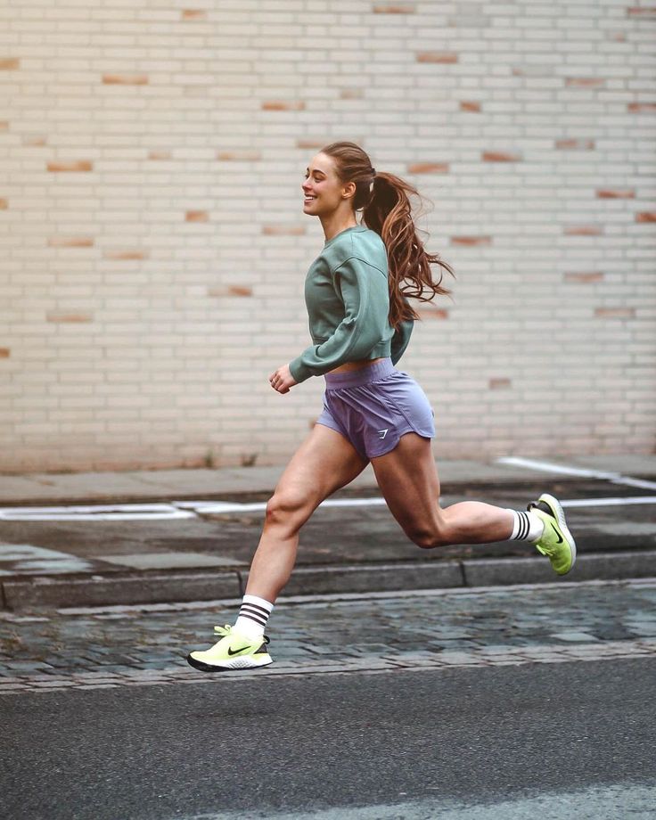 a woman is running down the street with her hair blowing in the wind and wearing shorts