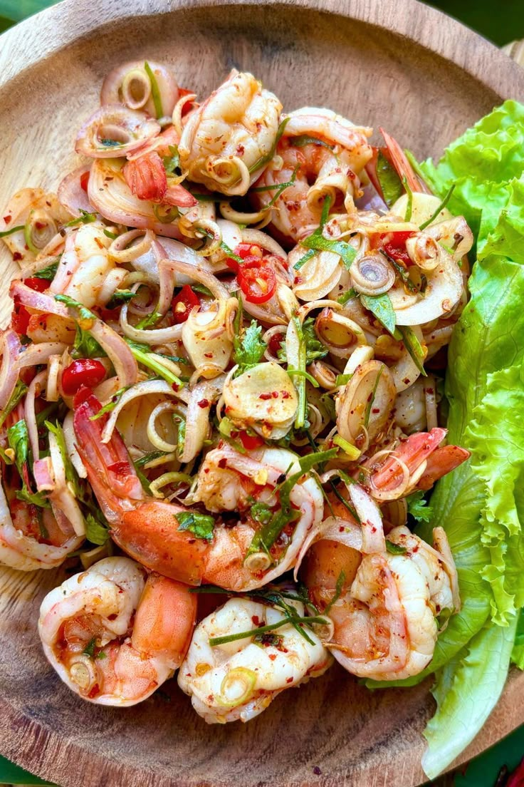 a wooden bowl filled with shrimp and veggies on top of lettuce