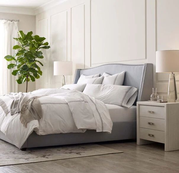 a bed with white sheets and pillows next to a potted plant in a bedroom