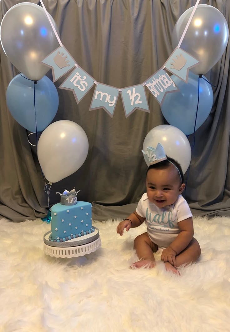 a baby sitting in front of a cake and balloons