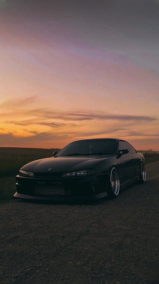 the car is parked on the side of the road near the grass and trees at sunset