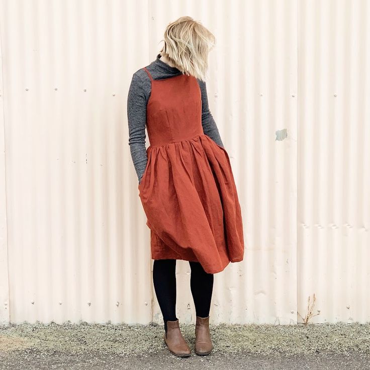 a woman standing in front of a white wall wearing an orange dress and black tights