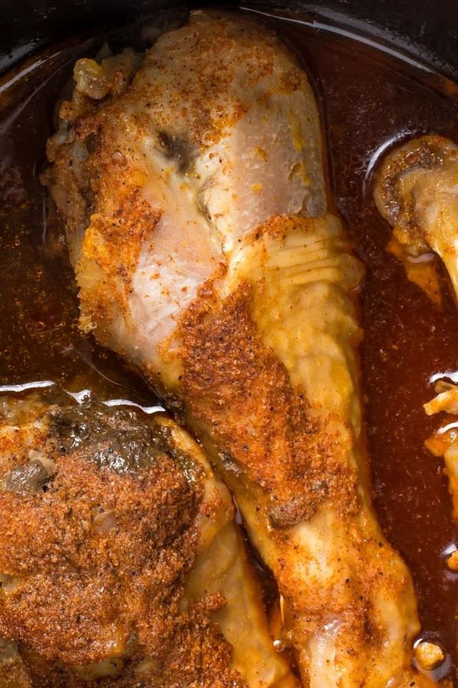 two pieces of cooked chicken in a slow cooker with brown gravy on top