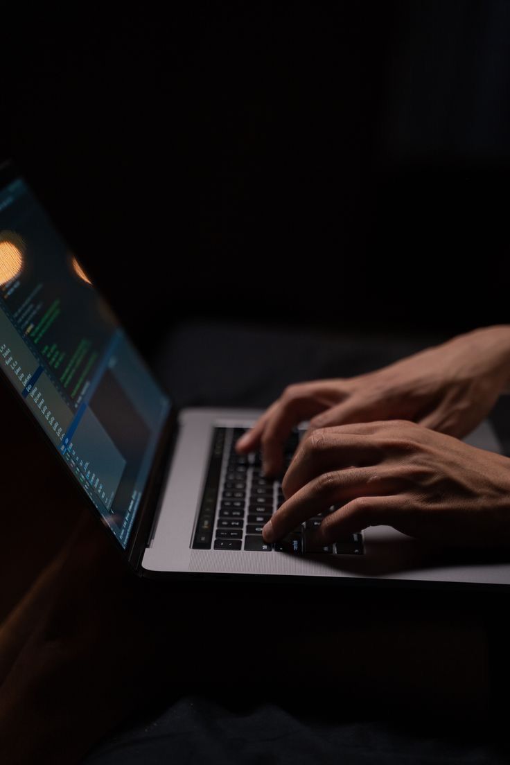 a person typing on a laptop in the dark with their hands resting on the keyboard