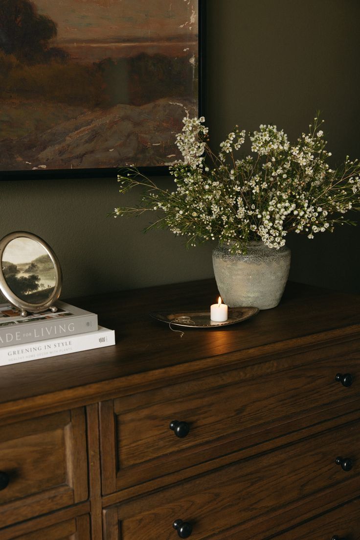 a vase filled with white flowers sitting on top of a dresser next to a mirror