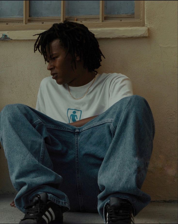 a young man sitting on the ground with his feet crossed and looking at something in front of him