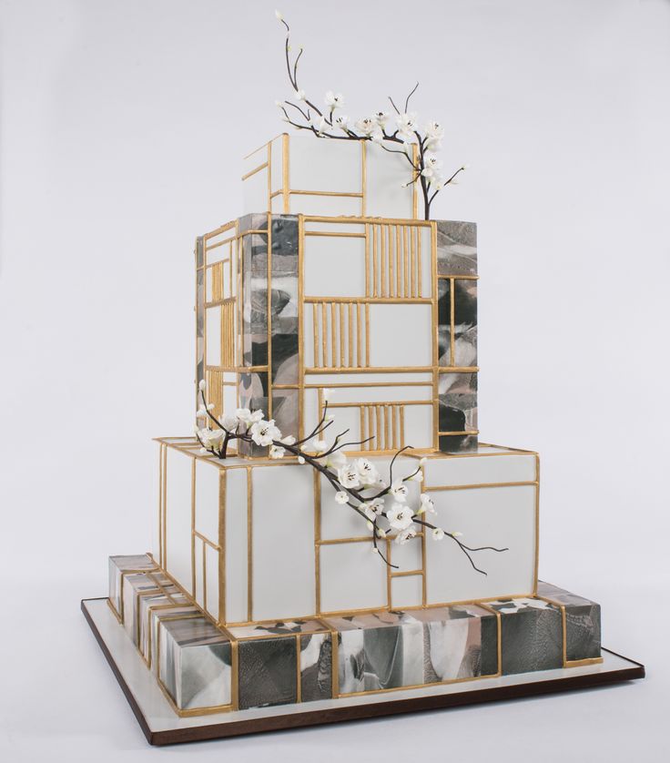 a three tiered cake decorated with white flowers and gold trimmings on a wooden stand