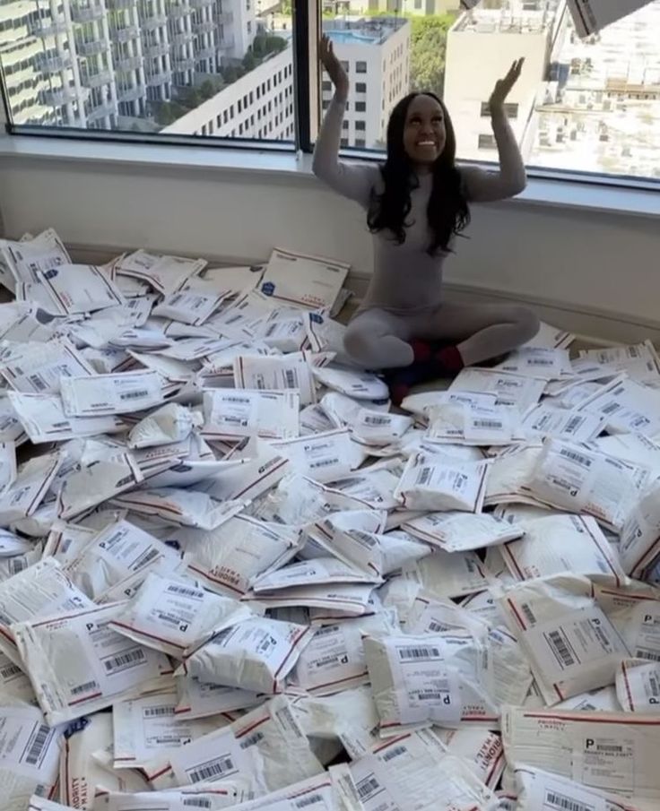 a woman sitting on top of a pile of mail in front of a large window