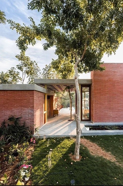 the house is made out of red bricks and has a large tree in front of it